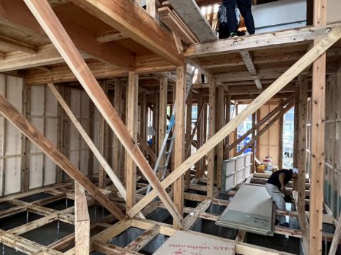 木材で組まれた骨組みがはっきり見える建設現場で、二人の作業員が施工している様子