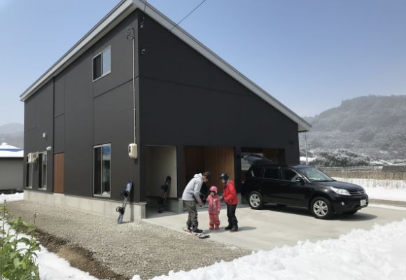 雪景色の中のモダンな家のガレージ前で、家族がウィンタースポーツの準備をしている様子