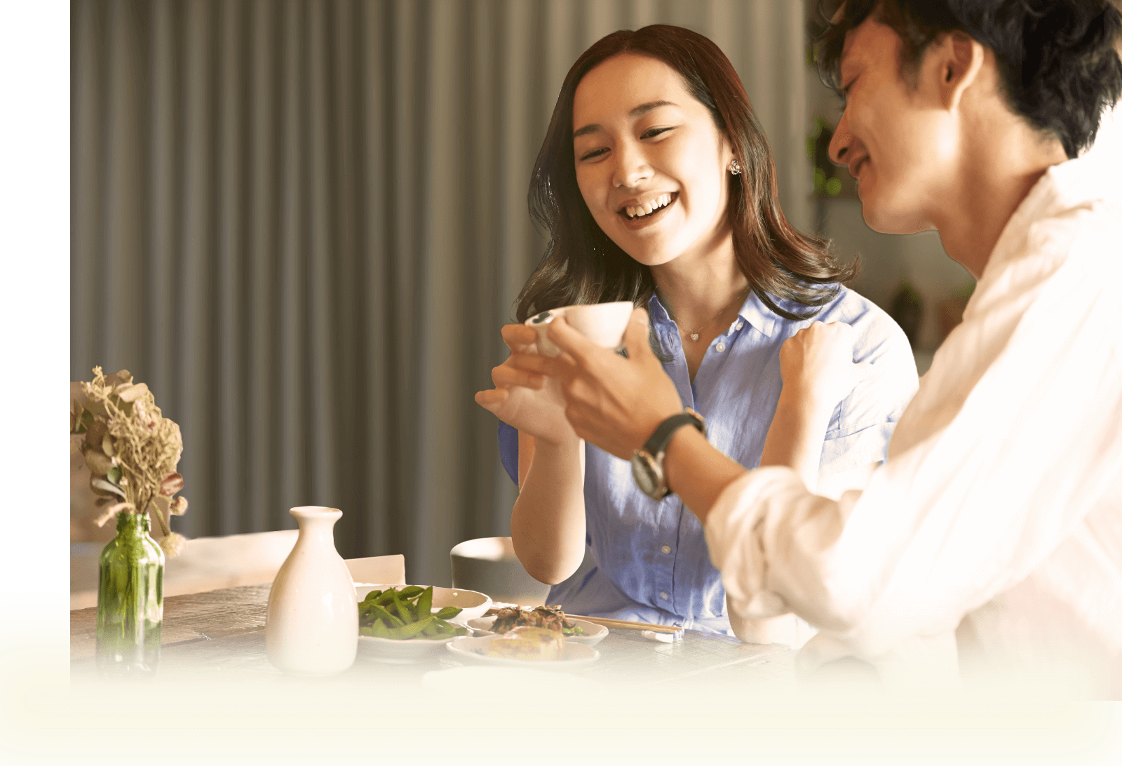 温かい室内で木目のテーブルに日本酒や枝豆を並べ、笑顔で和やかに語り合うカップルの様子