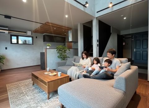 モダンなリビングのグレーのL字ソファで、父親・母親・男の子・女の子の一家がくつろぐ家族の様子