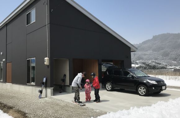 雪景色の中のモダンな家のガレージ前で、家族がウィンタースポーツの準備をしている様子